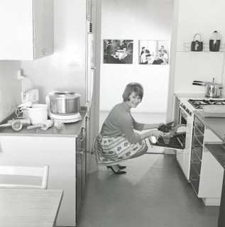 In the kitchen in the 1960s. A young woman in the kitchen taking out the ready baked breads from