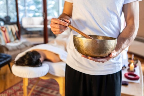 Massage therapist standing with a singing bowl in hands and giving a sound massage, to his client