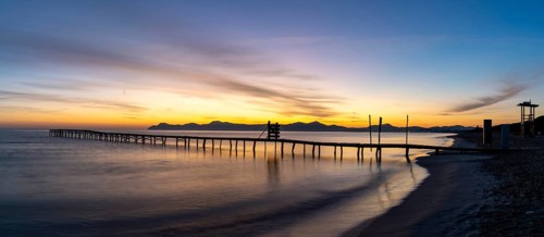 Peaceful sunrise seascape with an old wooden dock leading out into the calm ocean waters of Alcudia