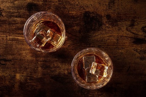 Whiskey in glasses with ice. Bourbon whisky on rocks on a dark rustic wooden background, overhead