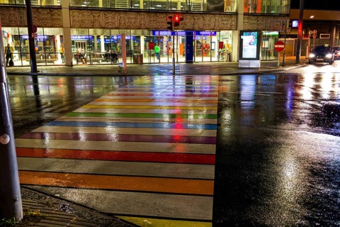 Rainy asphalt, zebra crossing in rainbow colours leads to the station, night shotLeoben, Styria,