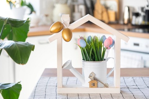 Key and tiny house of cozy home with Easter decor with color eggs on table of kitchen. Building,