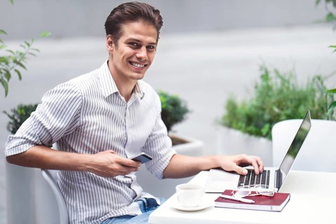 Smart attitude. Positive handsome man using a laptop and sitting in the cafe while surfing the