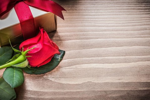 Present box with tied bow natural rose on wooden board