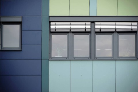 The modern façade of an office building with rows of windows and metal blinds