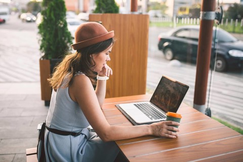 Beautiful young caucasian woman sitting on a terrace in a cafe in summer at a wooden table in a hat