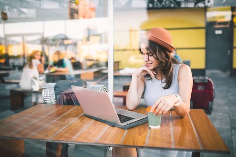 Beautiful young caucasian woman sitting on a terrace in a cafe in summer at a wooden table in a hat