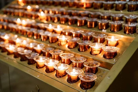 Votive candles burn in rows on a stand in the temple. Close-up.