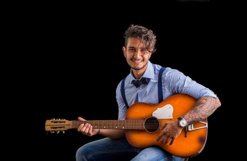 Handsome young man in bow-tie with guitar looking at camera.Studio shot