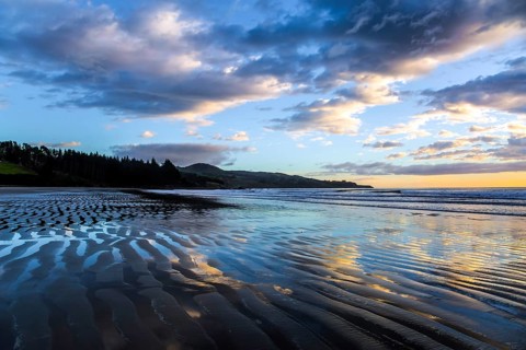 Strips of sand and water left by the ocean tide. Sunrise over the ocean. New Zealand, Pacific Coast