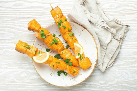 Grilled barbecue salmon skewers seasoned with green parsley and lemon on ceramic plate on white