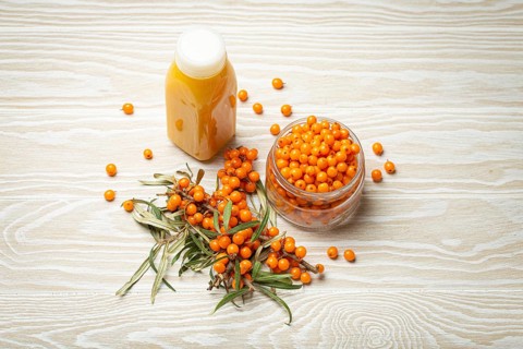 Sea buckthorn healthy drink in bottle, ripe berries in glass jar and branches with leaves top view