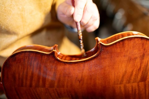 Luthier carefully varnishing a violin with a brush, showcasing the craftsmanship and meticulous