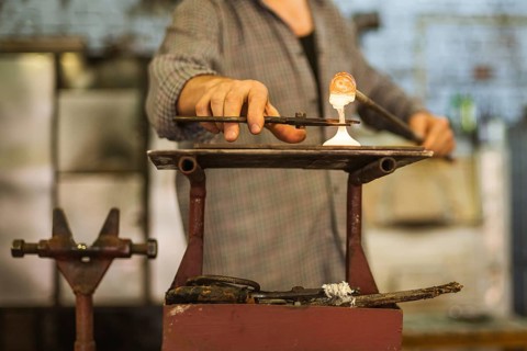 The worker makes a glass ornament in a glass smelter