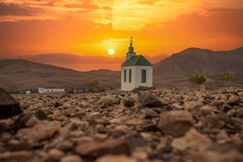 Small, sweet white wooden chapel in a barren volcanic landscape. Sunset, landscape shot of the