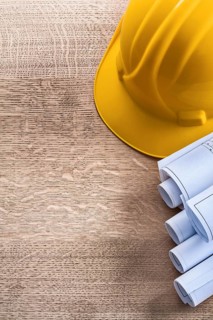 Construction helmet and blueprint rolls on wooden oaken board maintenance concept