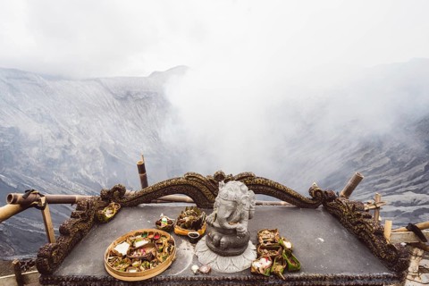 Traditional offerings and a statue on an altar with a misty volcano background, Bromo volcano, Sri