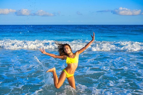 Bikini teen girl jumping happyt in Caribbean sunset beach splashing shore