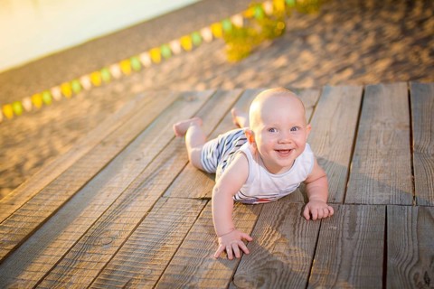 A child a boy, one year old, blond man lies on his stomach on wooden dock, pier in striped clothes,