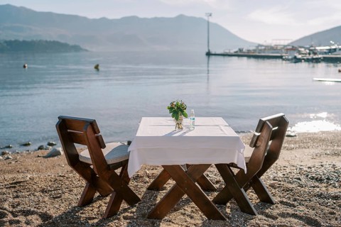 Laid table for two with chairs stands on a sandy beach by the sea.