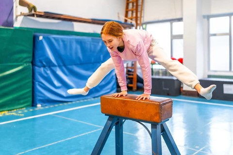 Female student performing gymnastic exercises on pommel horse during physical education class in