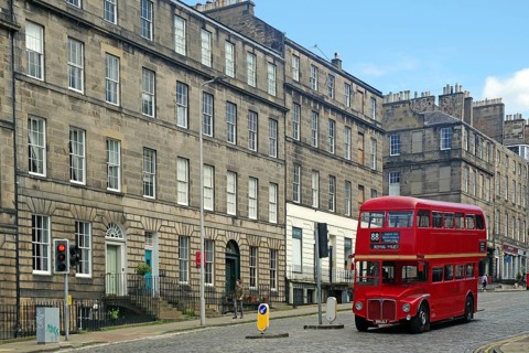 Red double-decker bus in historic old town with classic buildings and blue sky, Capital City,