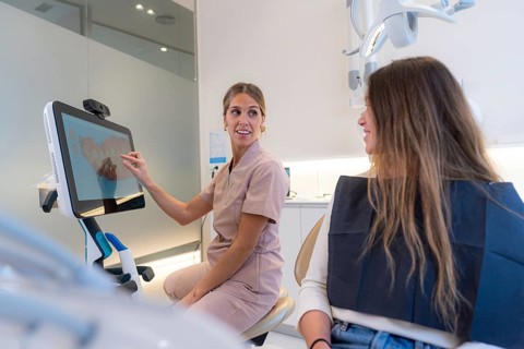 Dentist teaching 3d x-ray x-ray on monitor to young female client in modern dental clinic