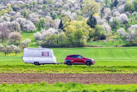 Car with caravan on the Albtrauf in the Lenninger Valley. Blossoming fruit trees in the orchards of