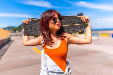Portrait of a urban confident asian woman holding a skateboard on shoulders standing in an urban