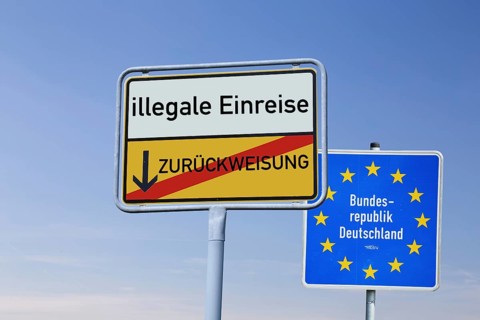 (Photomontage) Town exit sign with the inscription ILLEGAL ENTRY / REFUSAL in front of a border