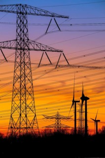High-voltage electricity pylons, transmission towers and wind turbines at sunset near the Borssele