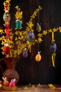 Branches of forsythia (Forsythia) in a rustic jug hung with Easter eggs against a dark background