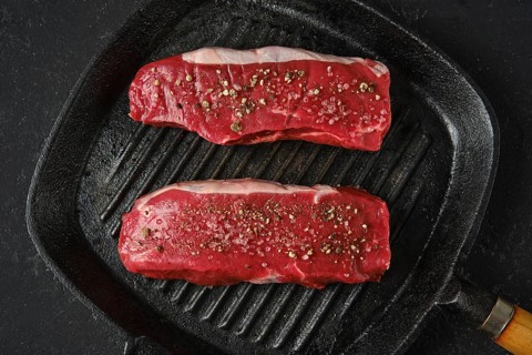 Top view of two thick cuts of raw beef steaks on a cast iron skillet. The marbled texture of the