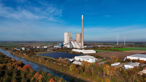 Industrial landscape with power plant and wind turbines, surrounded by autumn trees along a canal,