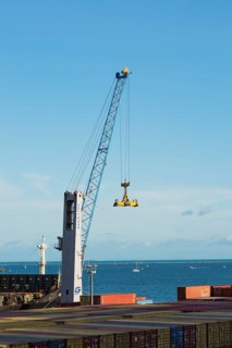 Gotwald crane with lifting attachment and stacked rectangular metal box shipping conatiners on dock