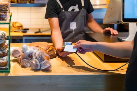 Customer in the bakery shop buying an artisan bread from the baker in the workshop, paying with the