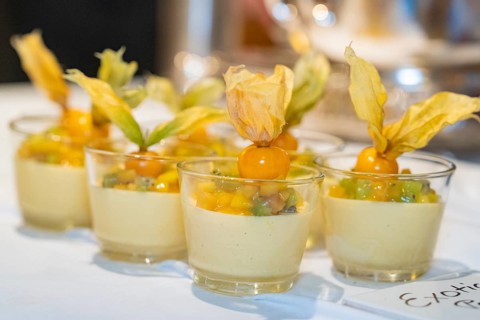 Small glasses with an exotic dessert of mango, kiwi and physalis on a white tablecloth,