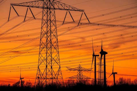 High-voltage electricity pylons, transmission towers and wind turbines at sunset near the Borssele