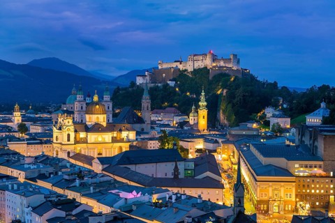 The city of Salzburg glows at dusk, dominated by the Hohensalzburg Fortress and the Alps, Salzburg,
