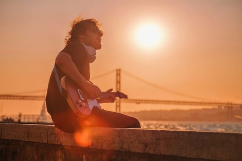 Hipster street musician in black playing electric guitar in the street on sunset