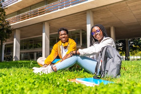 Portrait of two african university students relaxed on the grass of the campus smiling at camera