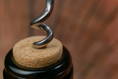 Metal corkscrew twisting into a cork in a wine bottle, ready to be opened