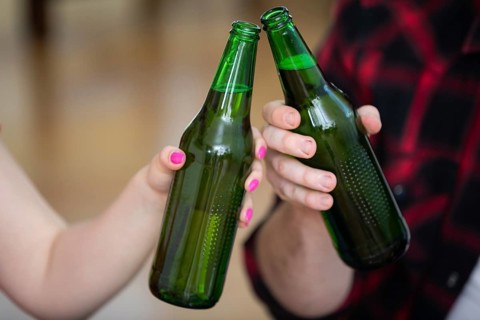 A close-up on the hands of two people. Each of them is holding a green bottle without a label. The