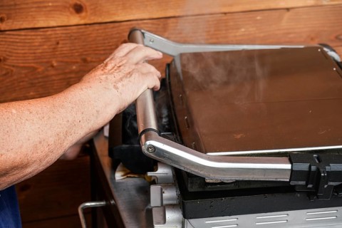 Senior hand closing metal electric grill, smoke coming up from grilled food inside, Pribylina,