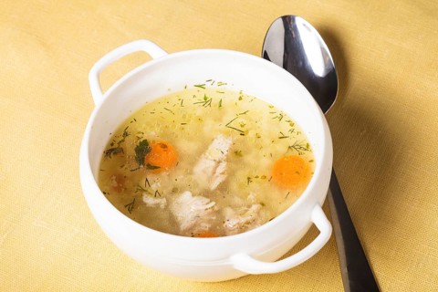 A chicken broth in white ware on the yellow tablecloth