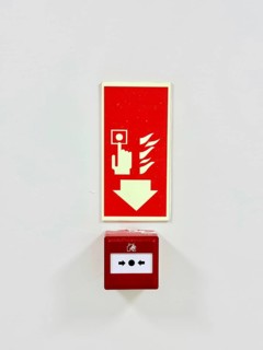 A red fire alarm button with an instructional sign above it on a white wall
