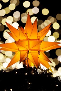 An orange-coloured, Christmassy star shines in the foreground in front of a beautiful, blurred
