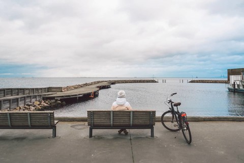 A young Caucasian woman sits with her back on a wooden bench overlooking the Baltic Sea on the