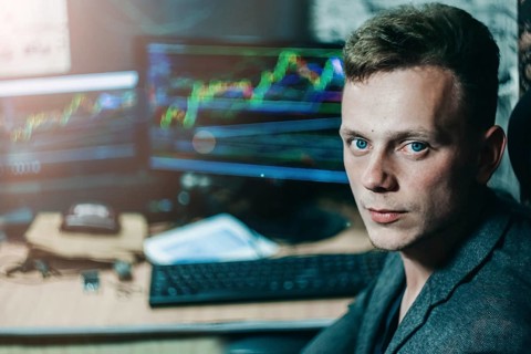 A man in an office setting with multiple monitors displaying graphs, suggesting a business