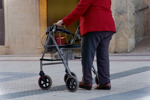 Elderly woman walking along a pedestrian street leaning on her wheeled walker